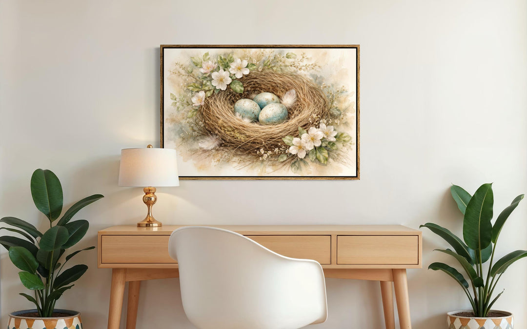 Bird nest wall art canvas print with blue eggs and spring florals hanging above a wooden desk.