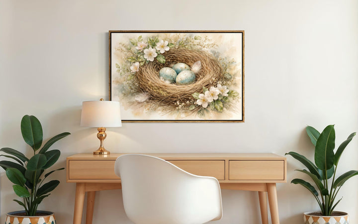 Bird nest wall art canvas print with blue eggs and spring florals hanging above a wooden desk.