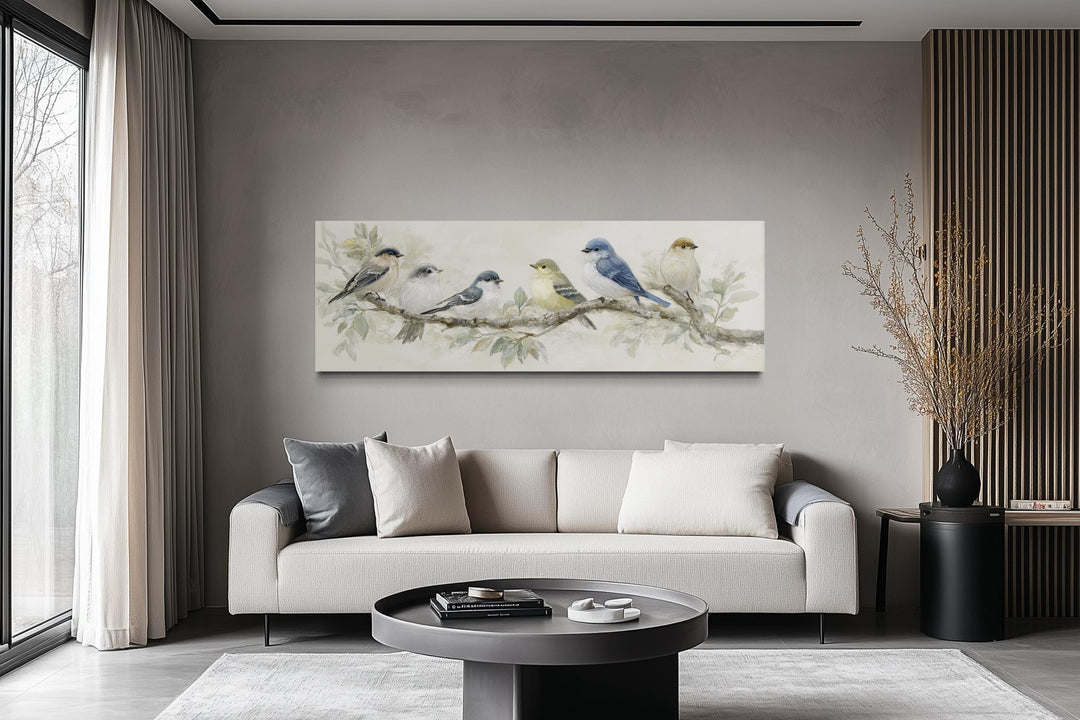 Panoramic canvas print of birds on a branch in neutral tones hanging above a modern sofa.