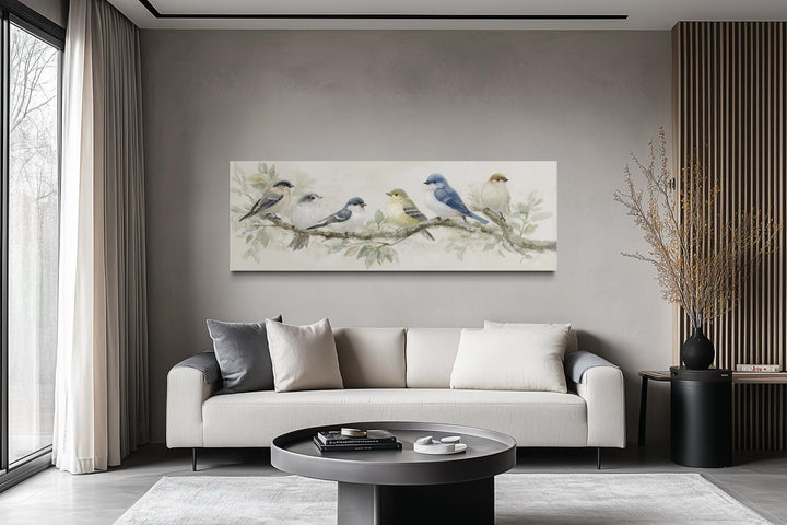 Panoramic canvas print of birds on a branch in neutral tones hanging above a modern sofa.