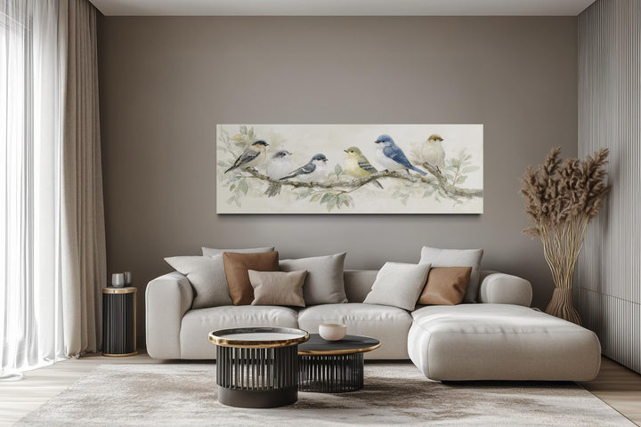 Panoramic canvas print of birds on a branch in neutral tones hanging above a modern sofa.