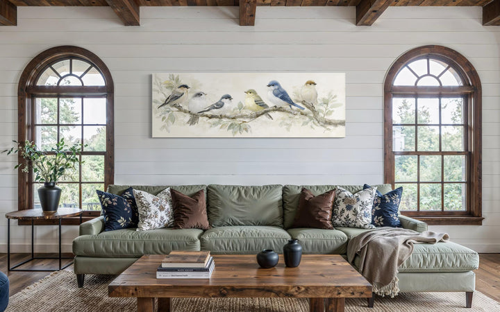 Panoramic canvas print of birds on a branch in neutral tones hanging above a green sofa.