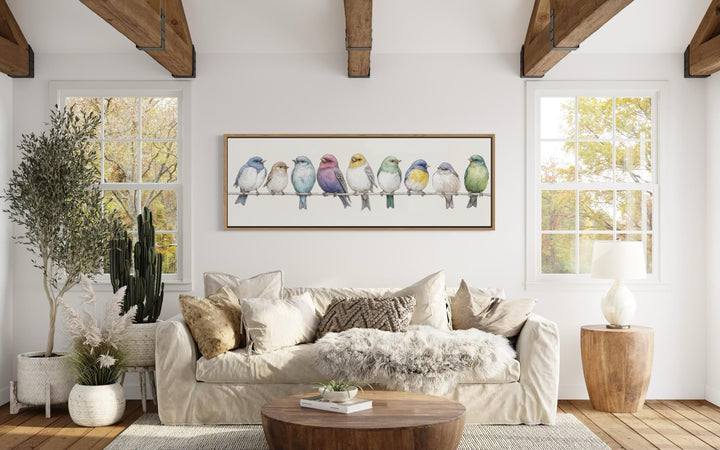 A long horizontal framed canvas of colorful songbirds on a wire in a modern farmhouse living room.