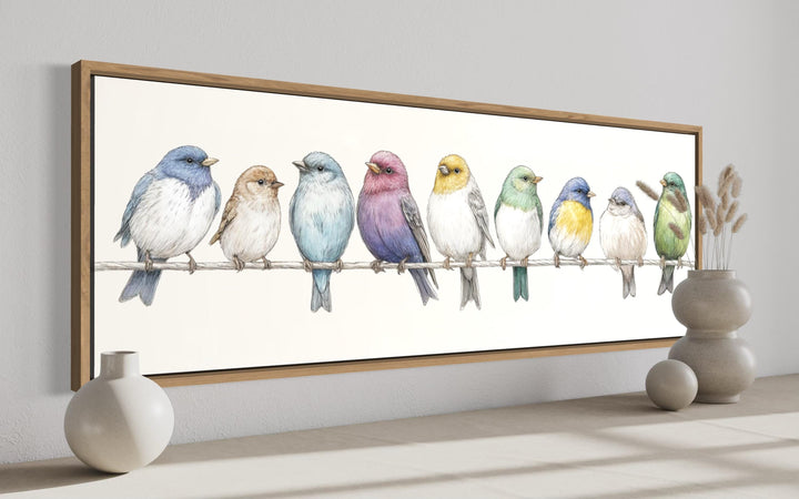 A long horizontal framed canvas featuring a row of colorful songbirds perched on a wire.