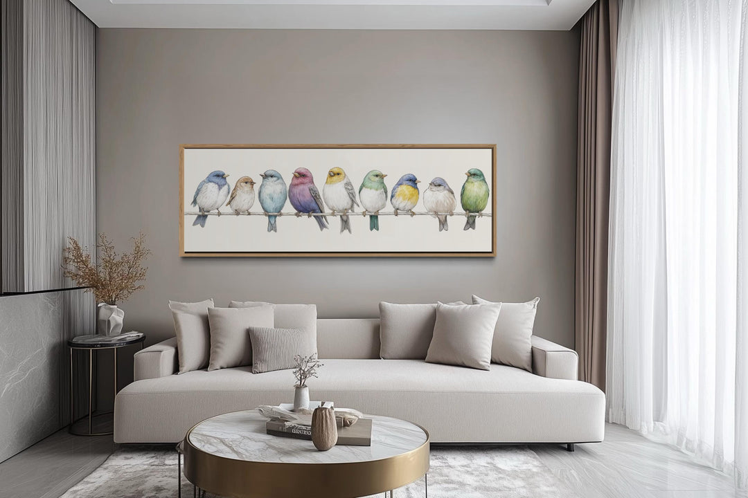 Colorful songbirds on a wire framed canvas art displayed above a modern sofa in a neutral room.