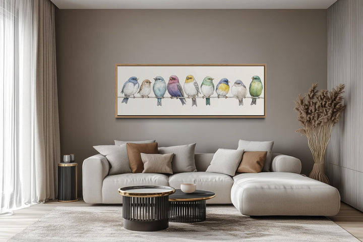 Colorful songbirds on a wire framed canvas art displayed above a modern sofa in a neutral living room.