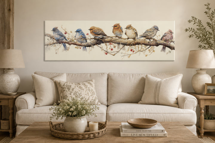 Horizontal framed canvas wall art featuring seven colorful birds perched on a branch above a sofa.