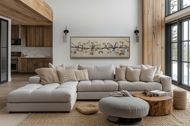 Panoramic birds perched on branch painting in a wood frame above a modern sectional sofa.