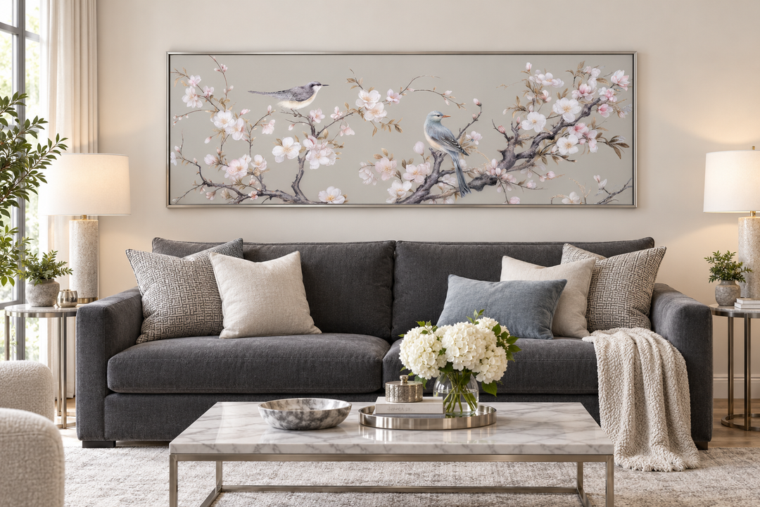 Horizontal framed canvas wall art featuring birds on blossoming branches above a grey sofa.