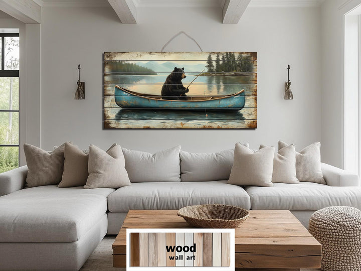 Rustic wood wall art featuring a black bear fishing in a blue canoe above a modern living room sofa.
