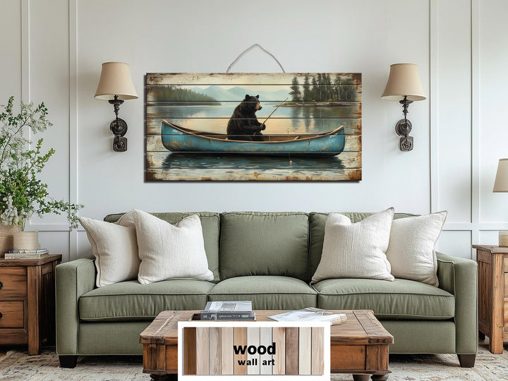 Rustic wood wall art featuring a black bear fishing in a blue canoe over a green sofa.