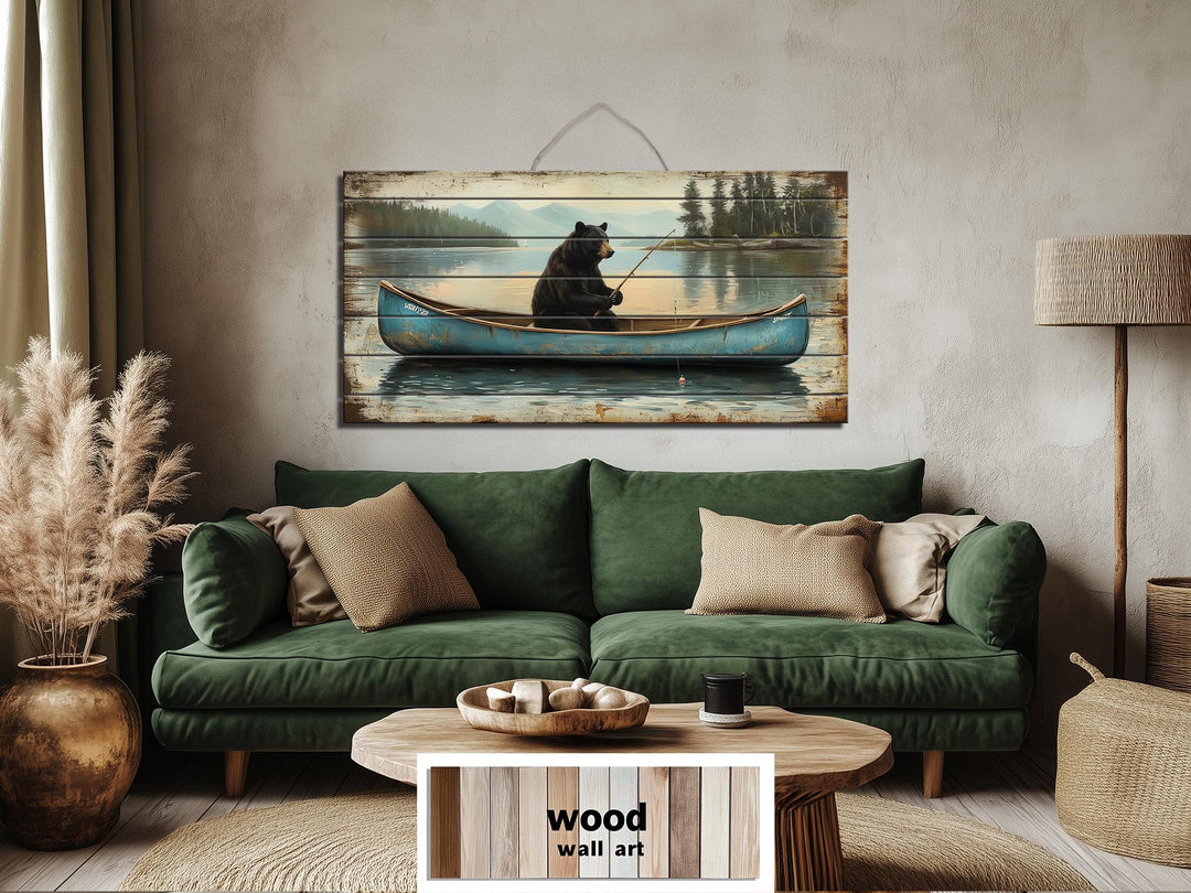 Distressed wood wall art featuring a black bear fishing in a blue canoe over a green sofa.