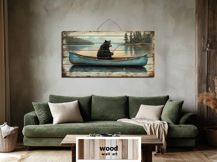 Rustic wood wall art featuring a black bear fishing in a blue canoe above a green sofa.