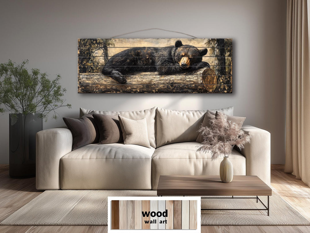 A wide horizontal wood wall art piece featuring a black bear sleeping on a log in a forest setting.