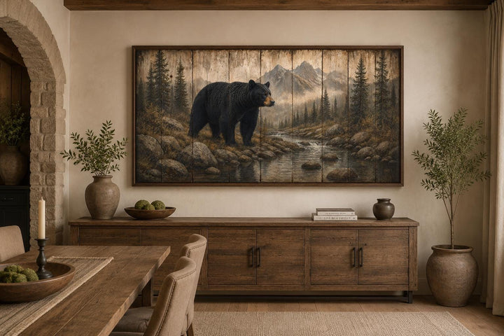 Black bear wall art canvas print in a rustic mountain forest scene above a wooden sideboard.