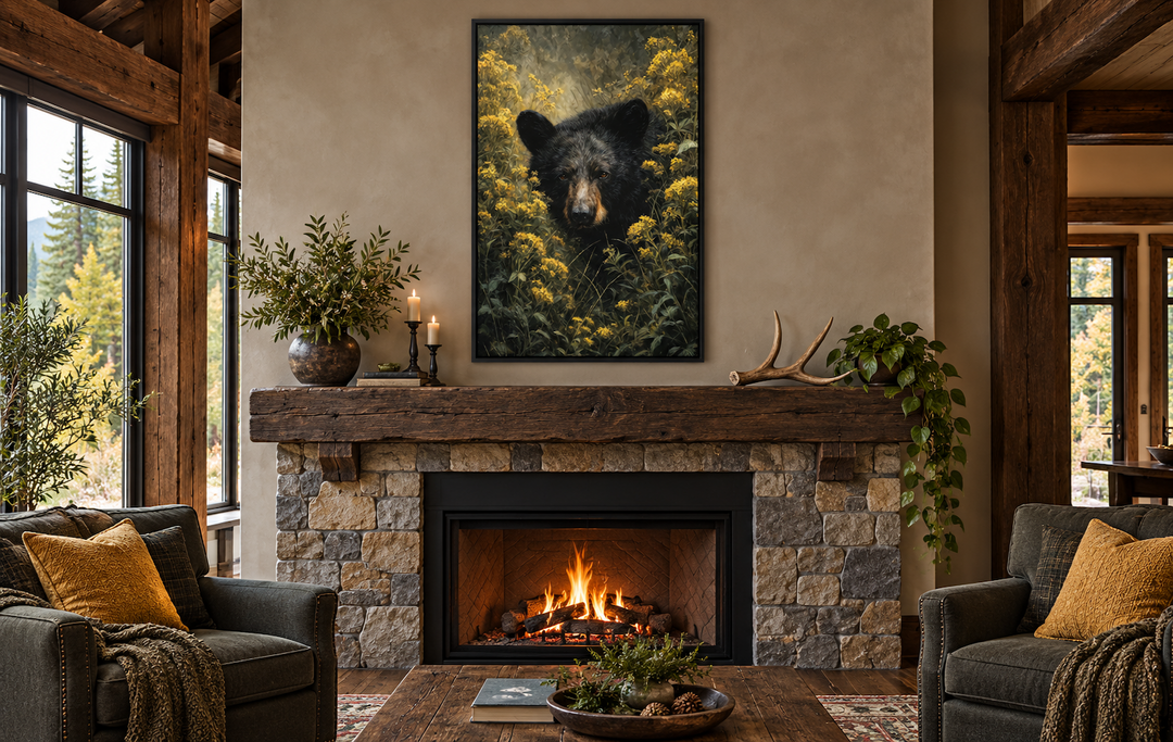 Black bear in yellow wildflowers framed canvas wall art hanging above a stone fireplace in a cabin.