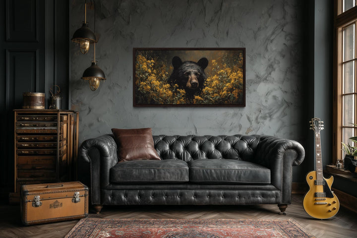 Black bear in yellow wildflowers canvas wall art above a black leather sofa in a rustic room.