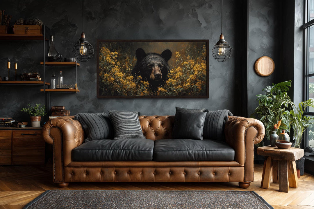 Black bear in yellow wildflowers canvas wall art hanging above a brown leather sofa in a dark room.