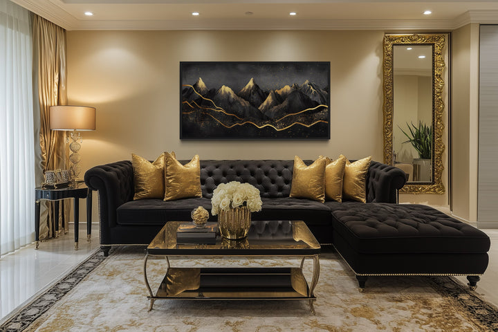Black and gold abstract mountain framed canvas wall art hanging above a black tufted sofa.