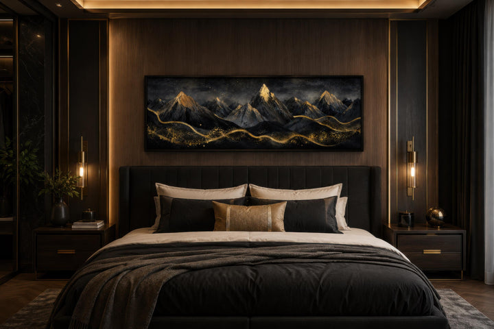 Long narrow canvas wall art featuring black mountains with gold accents above a dark bedroom headboard