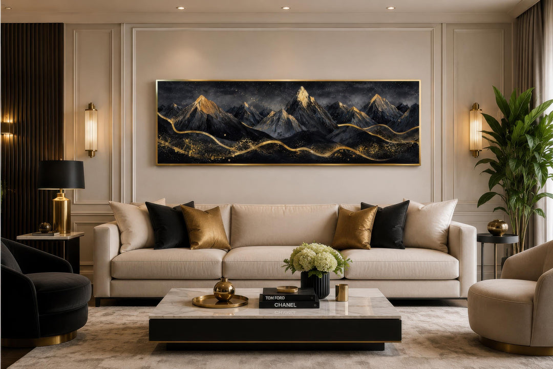 Long horizontal canvas art of black mountains with gold accents hanging above a beige sofa.