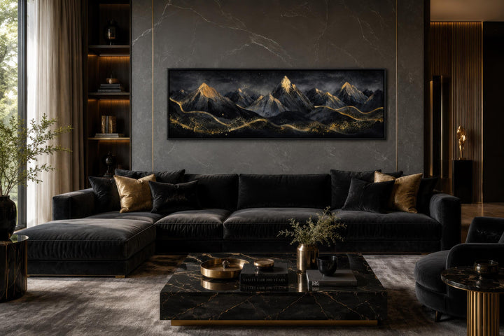 Long narrow canvas wall art featuring black mountains with gold accents above a dark velvet sofa.