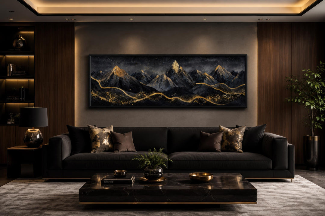 Long narrow canvas wall art featuring black and gold abstract mountains above a dark sofa.