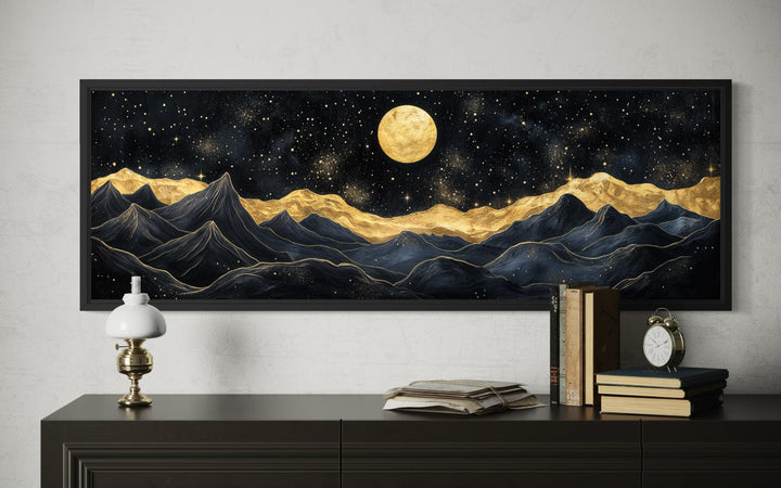 A framed horizontal canvas print of abstract black and gold mountains under a full golden moon.
