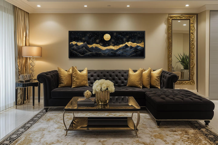 A panoramic canvas print of a moonlit mountain landscape in black and gold hangs above a sofa.