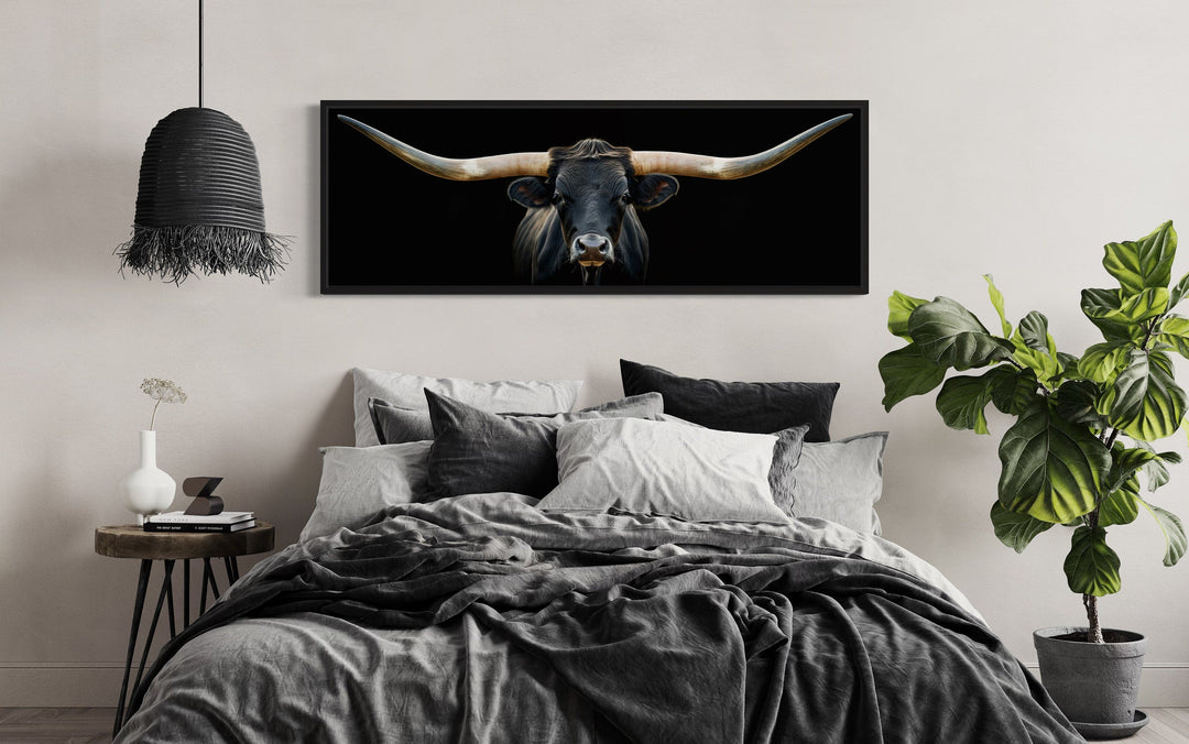 Panoramic framed canvas wall art of a black Texas longhorn steer hanging above a bed.