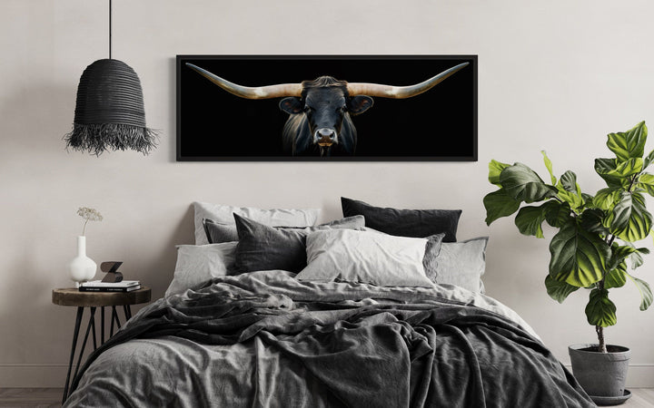Panoramic framed canvas wall art of a black Texas longhorn steer hanging above a bed.