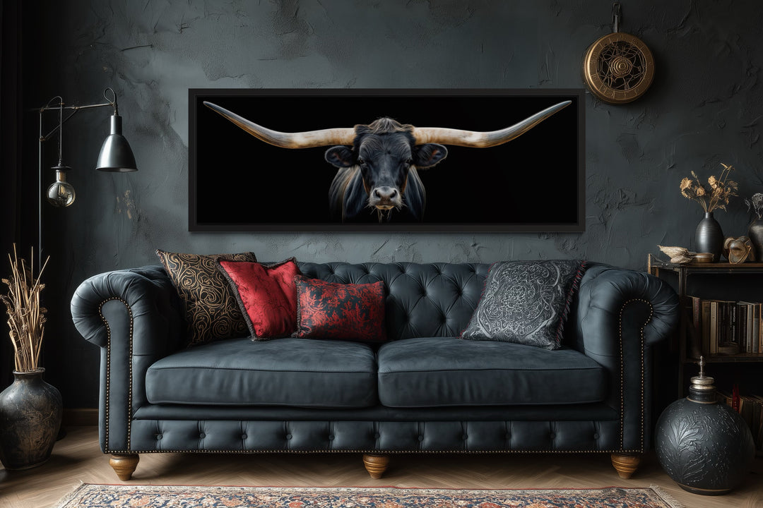 Panoramic framed canvas wall art of a black Texas longhorn steer hanging above a dark tufted couch.