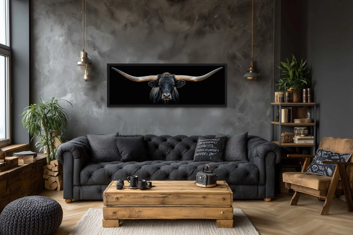 Panoramic framed canvas wall art of a black Texas longhorn steer hanging above a dark grey couch.