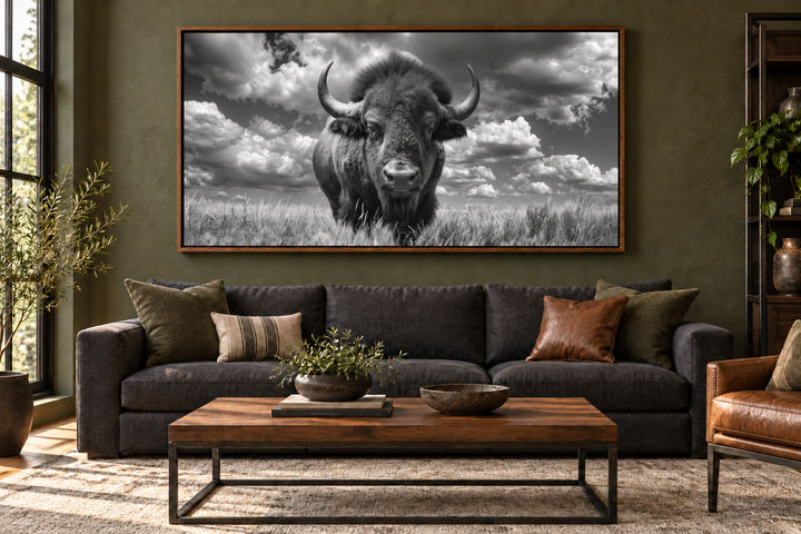 Black and white framed canvas print of a bison in a field, hung above a dark sofa in a rustic room.