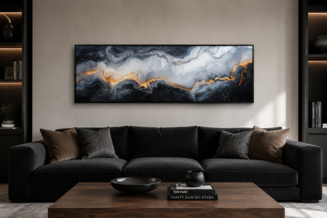 Long horizontal black, white, and gold marble abstract painting framed above a dark sofa.