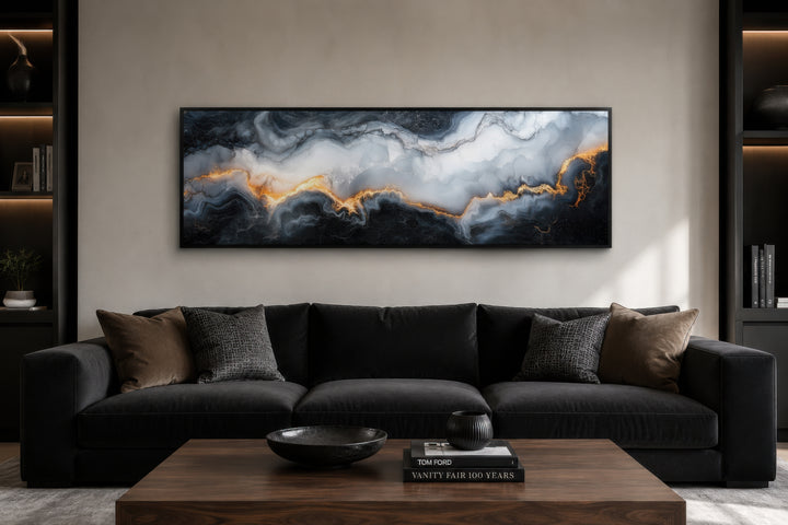 Long horizontal black, white, and gold marble abstract painting framed above a dark sofa.