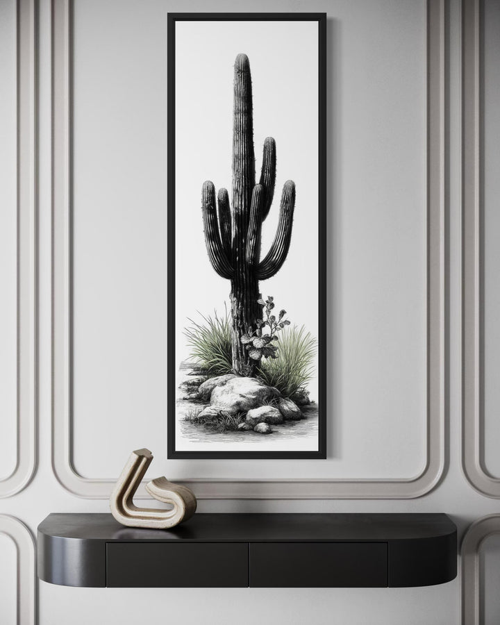 Tall narrow canvas art of a saguaro cactus in black and white with green accents on a paneled wall.
