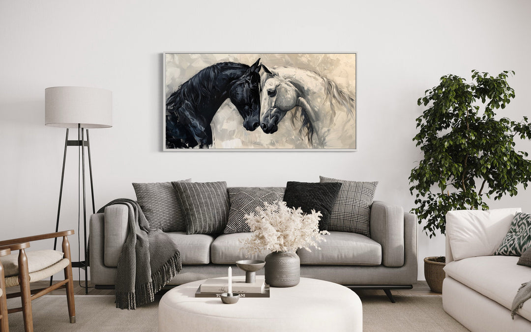 Framed canvas wall art of a black and white horse embracing, hung above a modern gray sofa.