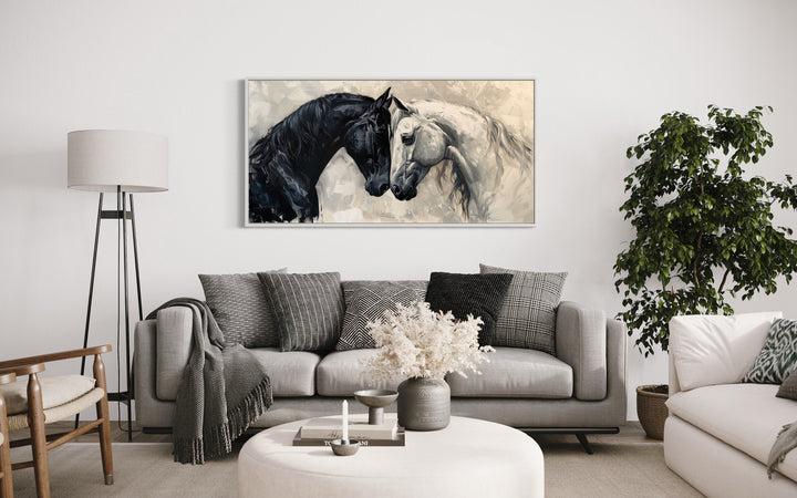 Framed canvas wall art of a black and white horse embracing, hung above a modern gray sofa.