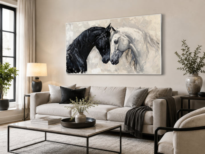 A large framed canvas of a black horse and a white horse touching heads above a modern sofa.