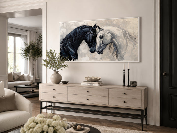 Framed canvas wall art of a black and white horse touching heads above a wooden sideboard.