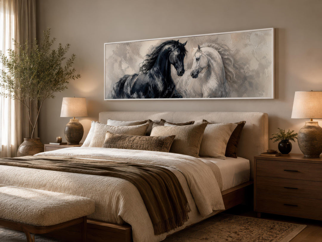 Black and white horses canvas print in a long horizontal frame above a bed in a neutral bedroom.