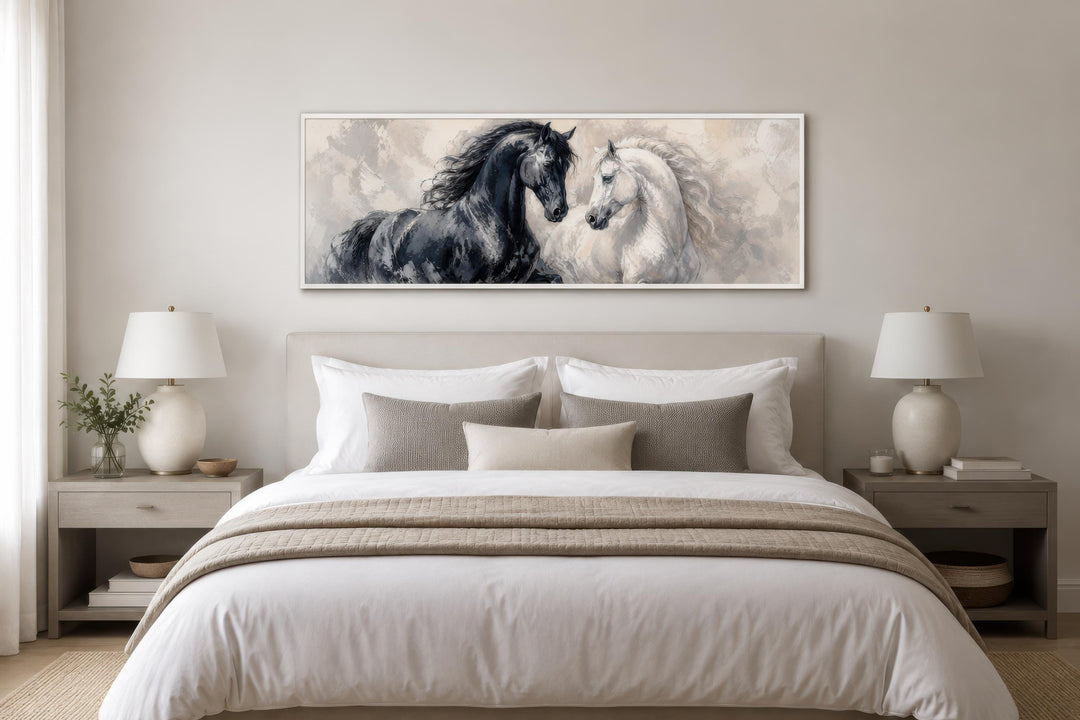 Black and white horses canvas print in a long horizontal frame above a bed in a neutral bedroom.