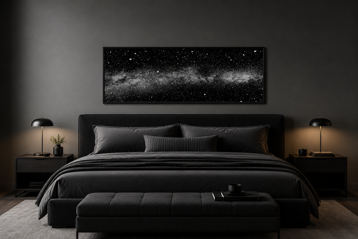 Framed black and white night sky canvas art above a dark bed in a modern bedroom setting.