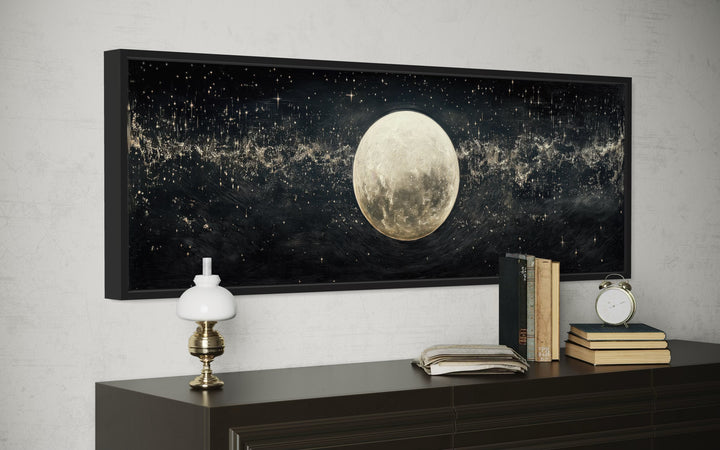 Black and white horizontal canvas art of a full moon in a starry sky, framed above a dark dresser.