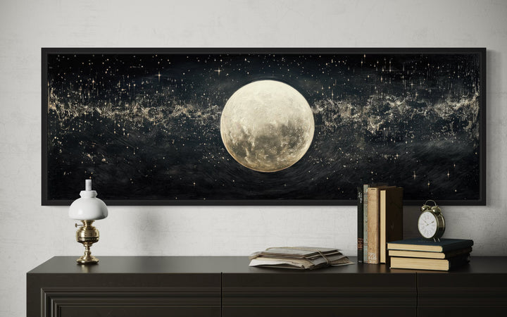 Horizontal black and white canvas art of a full moon in a starry sky above a dark wood dresser.