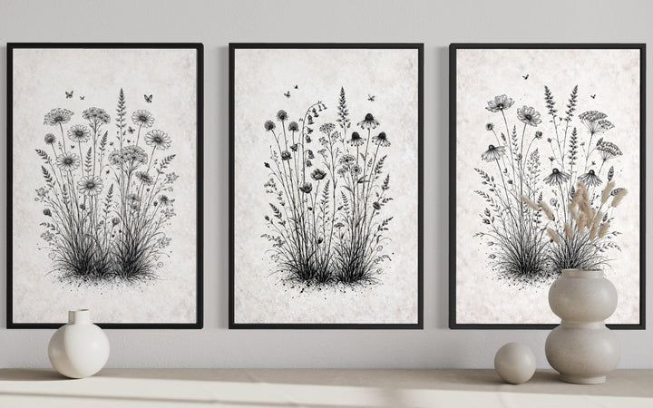 Three black and white wildflower botanical canvas prints in black frames on a neutral wall.