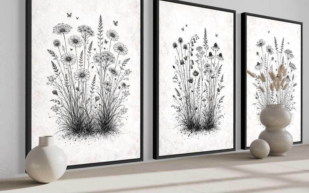Three black and white wildflower botanical canvas prints in black frames on a neutral shelf.