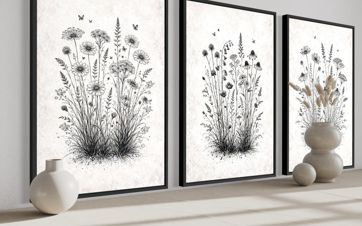 Three black and white wildflower botanical canvas prints in black frames on a neutral shelf.