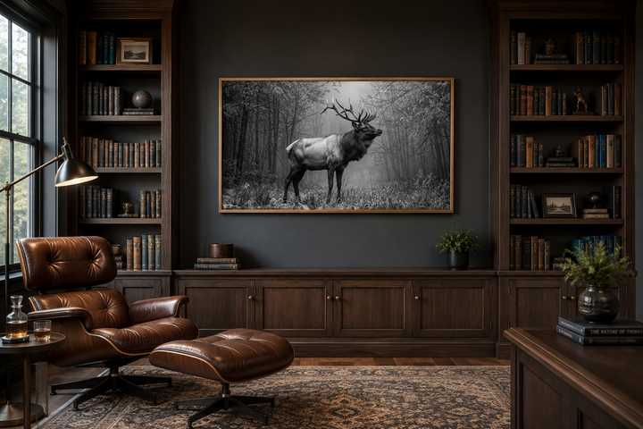 Black and white framed canvas wall art of an elk stag in a forest, hung in a dark wood library.